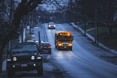 Yellow school bus on a quiet road, early morning commute scene with vehicles.